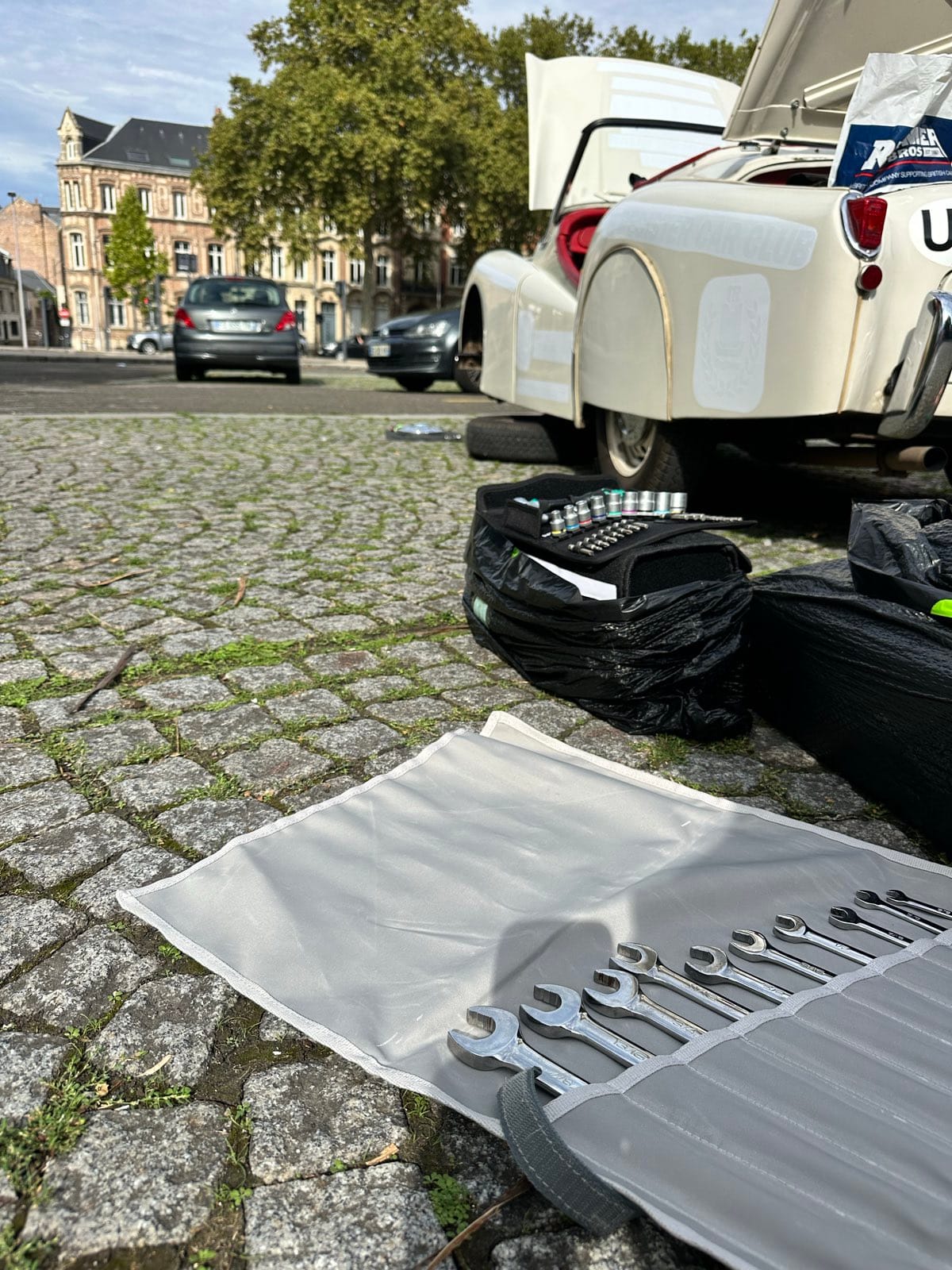 A spanner roll opened out on the cobbles with a socket set and tool bags beside it, TS2's tail and open boot behind