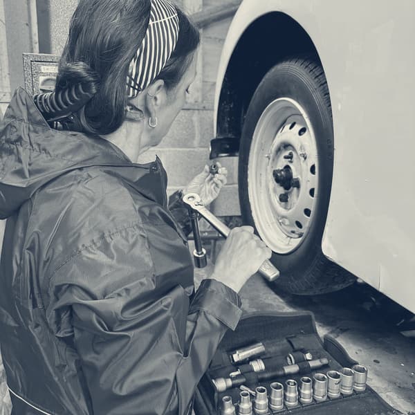 Evie at a wheel with a ratchet, a socket set laid open on the lift ramp beside her