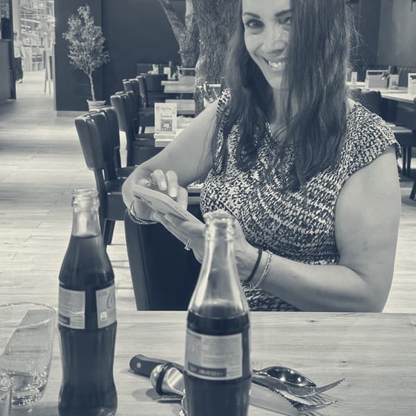 Evie at the restaurant table, smiling over a folded sheet of route notes, two bottles of cola in front of her