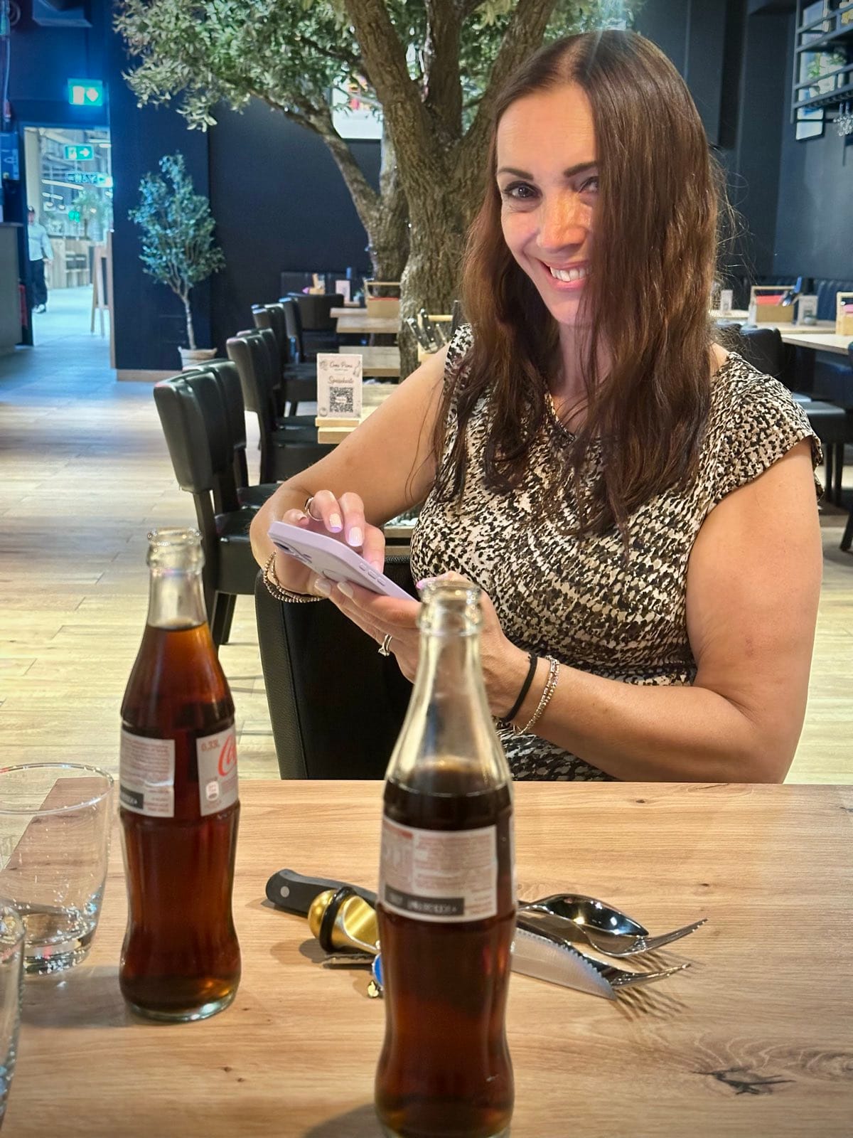 Evie at the restaurant table, smiling over a folded sheet of route notes, two bottles of cola in front of her