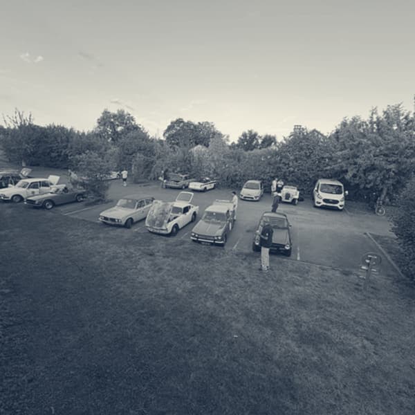 Triumphs parked in rows on a hotel car park at first light, seen from an upstairs window, people standing about between them