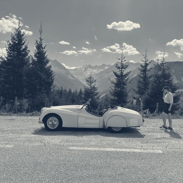 TS2 side on at an Alpine viewpoint, spruces and snow streaked peaks behind her