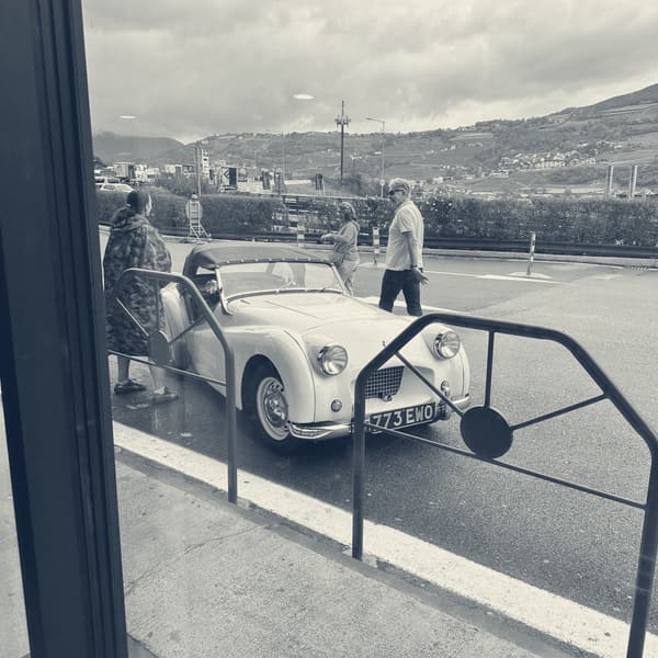 TS2 parked outside the services seen through the window, people gathered around her, vineyard slopes behind