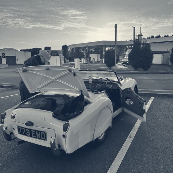 TS2 at Aldi with her boot lid up and Evie leaning into it, the sun coming up orange behind the canopy