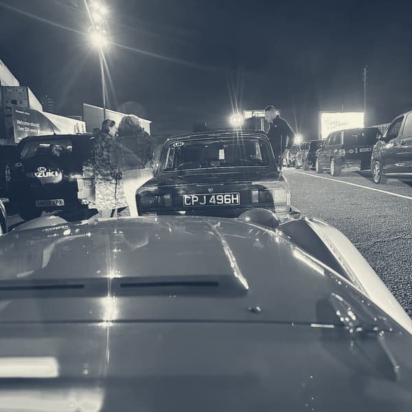 TS2's bonnet in the foreground of the night-time ferry queue at Portsmouth, a blue Triumph 2000 ahead of her under the floodlights